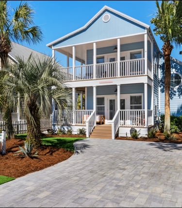 Luxury blue two-story beach house rental with a paved driveway and palm trees.