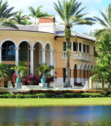 Luxury waterfront Mediterranean villa with white arches and tall palm trees reflected in the lake.