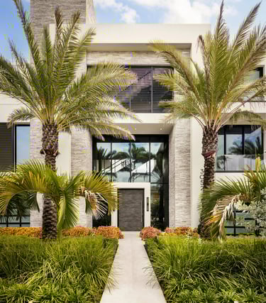 Modern luxury home exterior with stone accents, palm trees, and a white stone walkway.