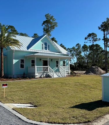 New light blue coastal home with a metal roof, front porch, and palm tree on a grassy lawn.