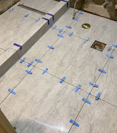 Pose de carrelage grand format avec croisillons autonivelants dans une salle de bain en rénovation