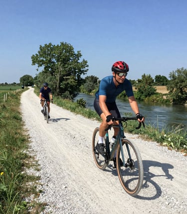 Cyclist on a gravel bike riding along a sunlit country road lined with vineyards.
