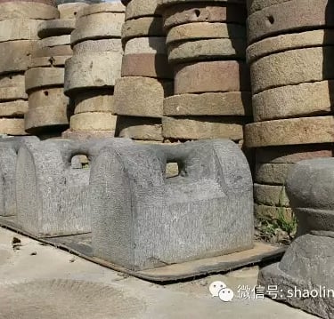 Ancient Chinese stone strength training equipment and stacked millstones at a Shaolin martial arts temple.