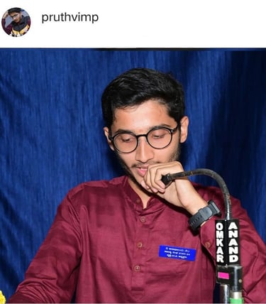 Pruthvi M P in a red shirt and glasses is holding a microphone