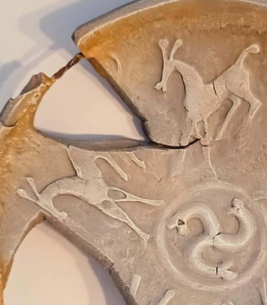 Close up of a bowl-like sculpture with embossed horse figures and symbols in rust/brown hues