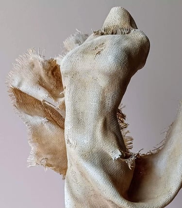 Close up image showing a clay and canvas sculpture of a female torso with windswept, ragged clothes.