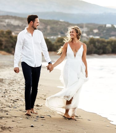 Una coppia di sposi cammina tenendosi per mano su una spiaggia, i loro sguardi teneri si incrociano