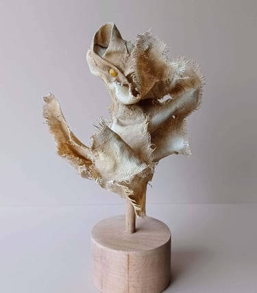 Rear view, showing a clay and canvas sculpture of a female torso, with windswept, ragged clothes.