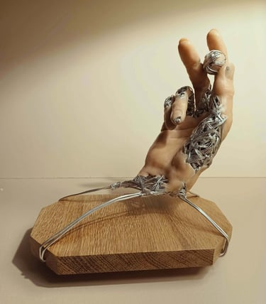 A sculpture of a single hand, part wire, part flesh coloured clay holding a small wire and clay ball