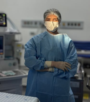 mulher branca em sala de cirurgia paramentada de braços cruzados olhando na direção da camera com um foco de luz em seu rosto
