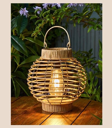 Decorative solar rattan lantern with a glowing Edison bulb on a wooden outdoor table.