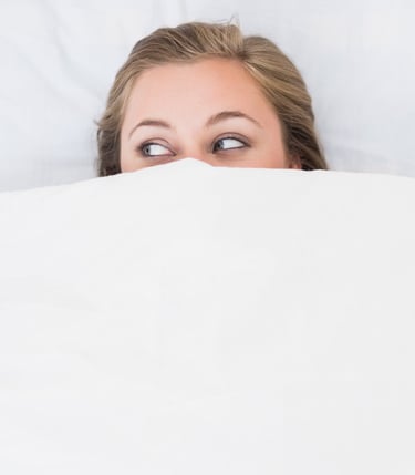 a woman is peeking behind a blanket in a bed