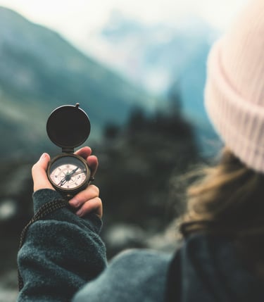 woman's hand holding compass in front of blurry nature backdrop