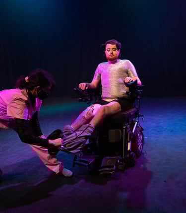 A person in pink scrubs pulls trousers off Jamie Hale, who sits in their wheelchair