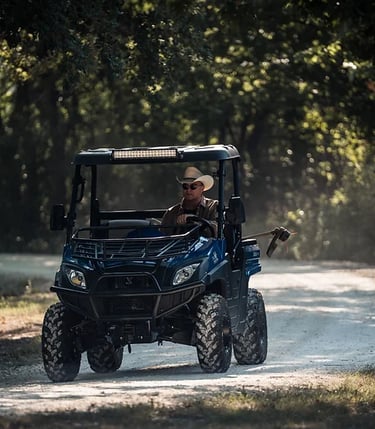man in cowboy hat driving a huntve utv with a weed trimmer in the back