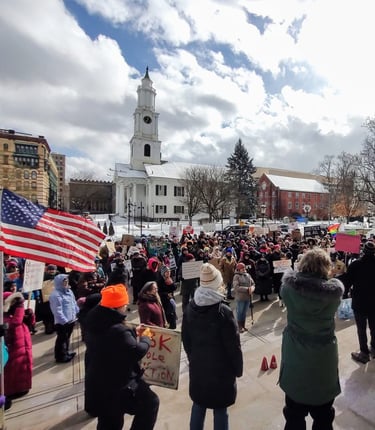 Group of people rallying on a cold snowy day. A church in the background. An American flag flying. 