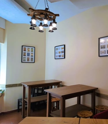 Zona interior del Bar Las Tinajas Huelva, con mesas altas, cuadros en la pared, lámpara colgante y planta decorativa.