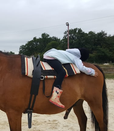 Enfant allongée sur le dos de son cheval lors d'une séance d'équithérapie