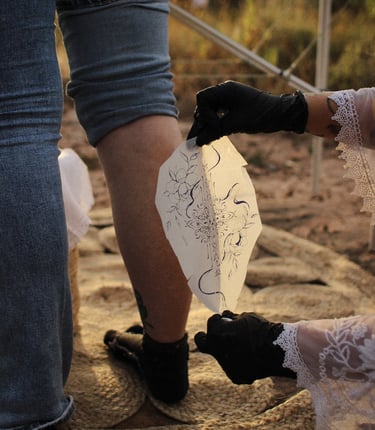 un calque de tatouage est posé sur un mollet, dans une ambiance aux couleurs chaudes