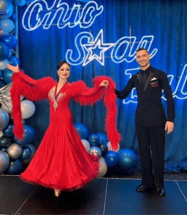 A ballroom couple performing a bow, with the man in a black suit presenting the woman in a red dress