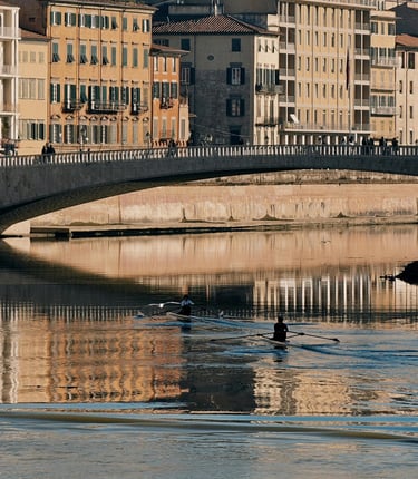 Rowers on the Arno River with colourful buildings and bridge in Pisa, Italy.