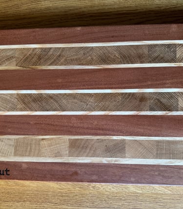 Handmade wooden cutting board with a striped pattern of mahogany and maple wood grain on a table.