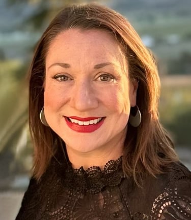 Professional headshot of a smiling woman with red lipstick, brown hair, and a black lace top.