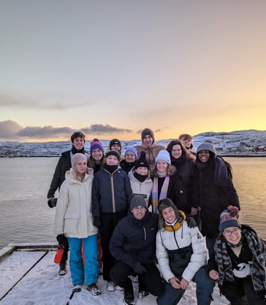 a group of people standing on a dock with a boat and beautiful sunset in the Nordic background