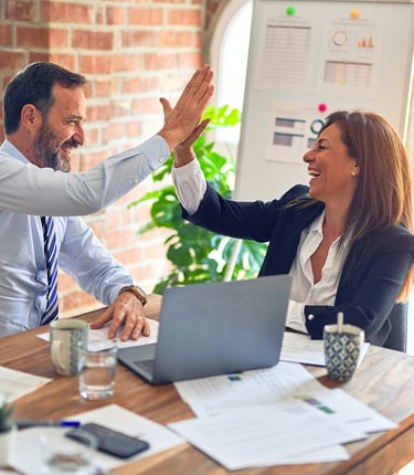 businessman and businesswoman at desk, high-fiving each other