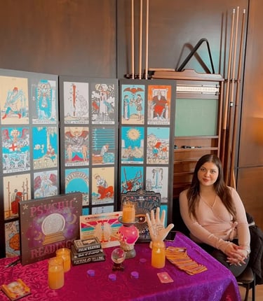 Professional psychic sitting at a fortune telling table with tarot cards, candles, and a palm reading hand.