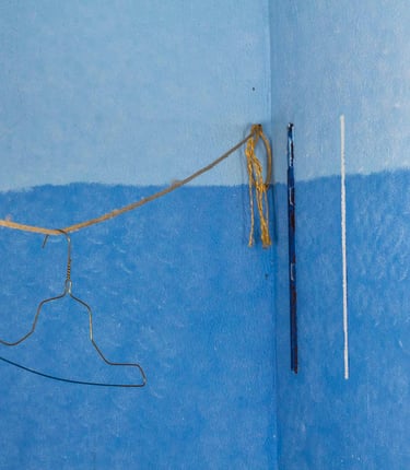 Golden bent clothing hanger dangling from a rope in a blue painted room. 