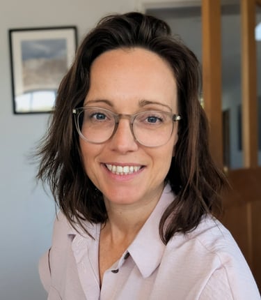 A professional female tutor with brown hair and clear-framed glasses smiling.