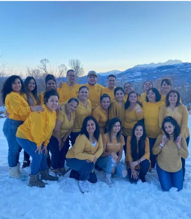A group of diverse people in yellow shirts posing together in the snow with mountain scenery.