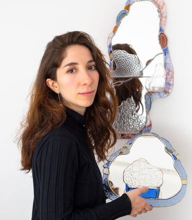 Artista sosteniendo un espejo artesanal de vitral con forma orgánica y un borde de mosaico