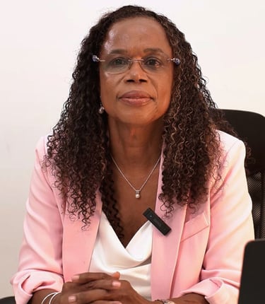 Professional woman with curly hair wearing a pink blazer and glasses in an office setting.