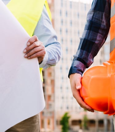 Dupla de construtores onde vemos um com um capacate na mão e outro segurando um projeto