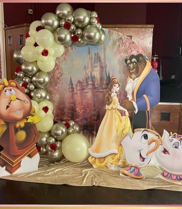 Beauty and the Beast party decorations featuring a gold balloon arch and character cardboard cutouts.