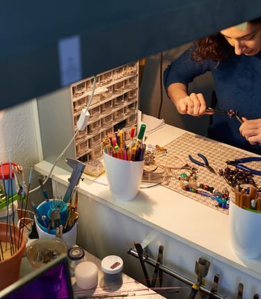 Fabricante de joyas que utiliza alicates para elaborar collares de cuentas hechos a mano en un banco