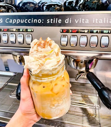 a person holding a jar of ice latte with whip cream by espresso machine
