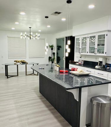 A modern kitchen with white cabinets, a large island, and a dining table, decorated with vases, book