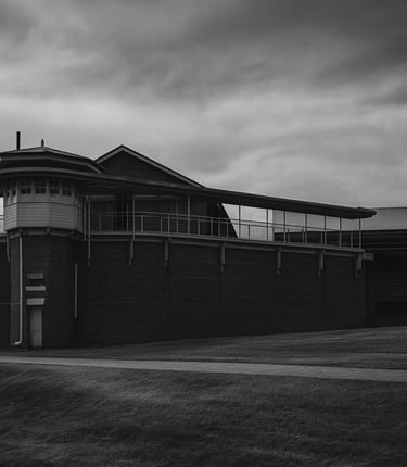 Black and white photo of Boggo Road Gaol with dark skies, creating a moody, haunted atmosphere.