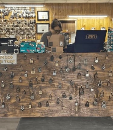 Emily, a female locksmith, assisting customers at the front counter of Jack's Locksmith in Burnsville, NC, wall of locks