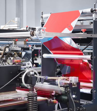 Industrial automated packaging machine processing red metallic film for high-speed manufacturing.