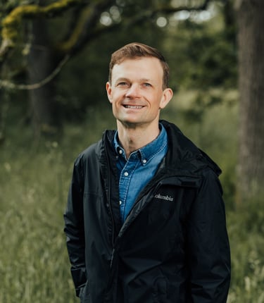 Jesse Robertson in a blue collared shirt and black rain jacket in a Garry Oak meadow.