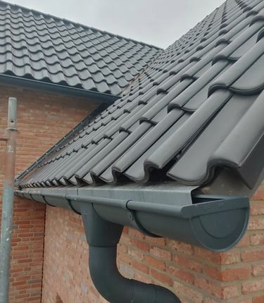 Toiture en tuiles noires avec gouttière en PVC anthracite – finition soignée sur façade en briques.