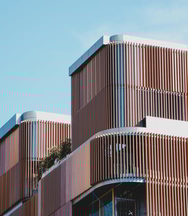 Edificio moderno construido con hormigón, vidrio y revestimiento de madera, con mucha vegetación.