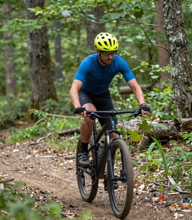Cyclist riding a mountain bike on a rugged forest trail with sunlight filtering through trees.