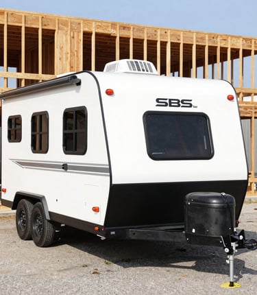 A sleek, dark teal and safety orange branded travel trailer parked at a rugged job site under a clear sky.