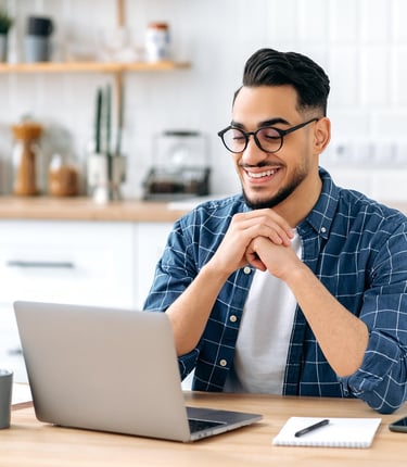 Man sitting at kitchen table, smiling happily towards his laptop