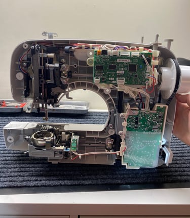 A sewing machine with the outside covers removed, revealing the inside of a computerized machine. 